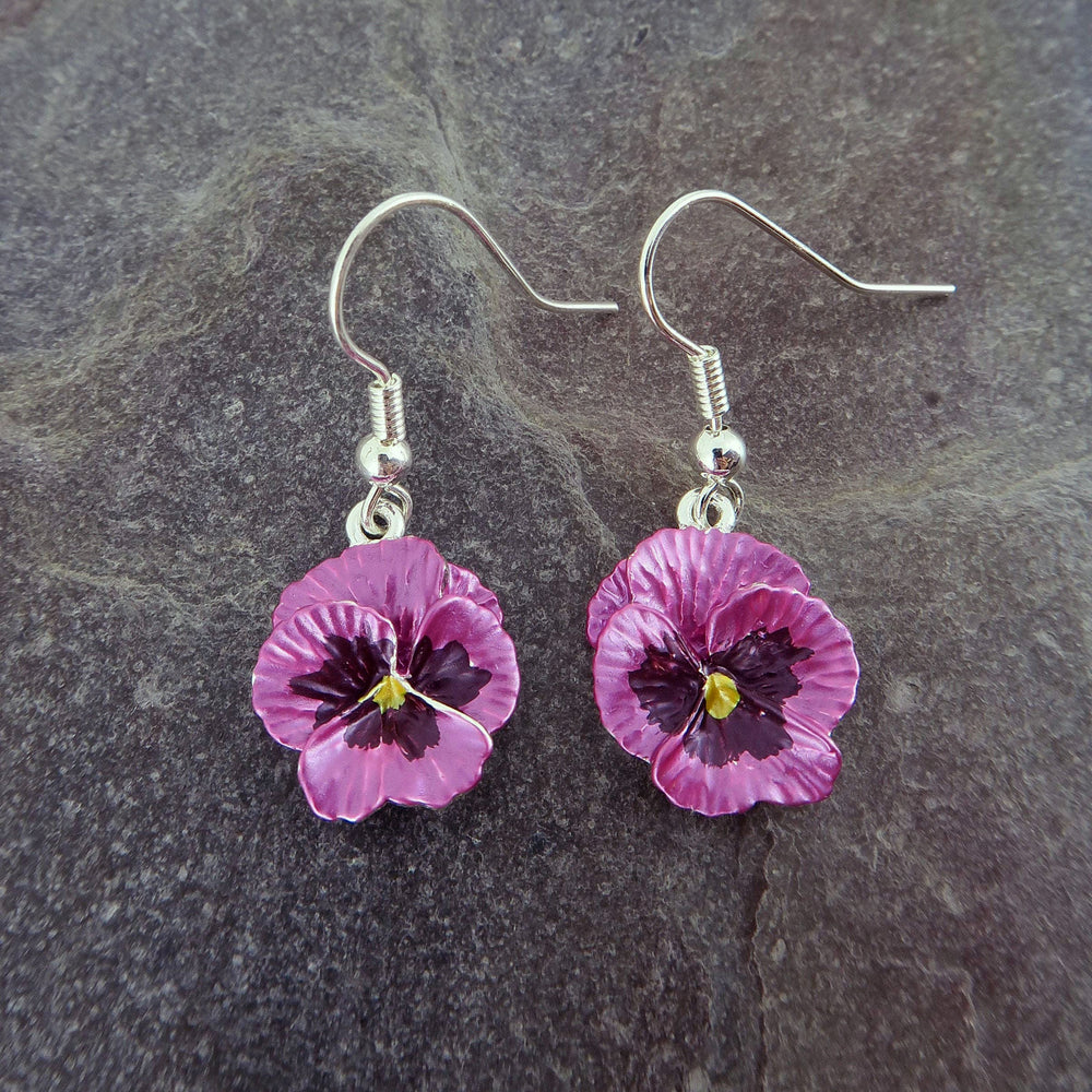 Purple flower-shaped earrings on a dark stone surface