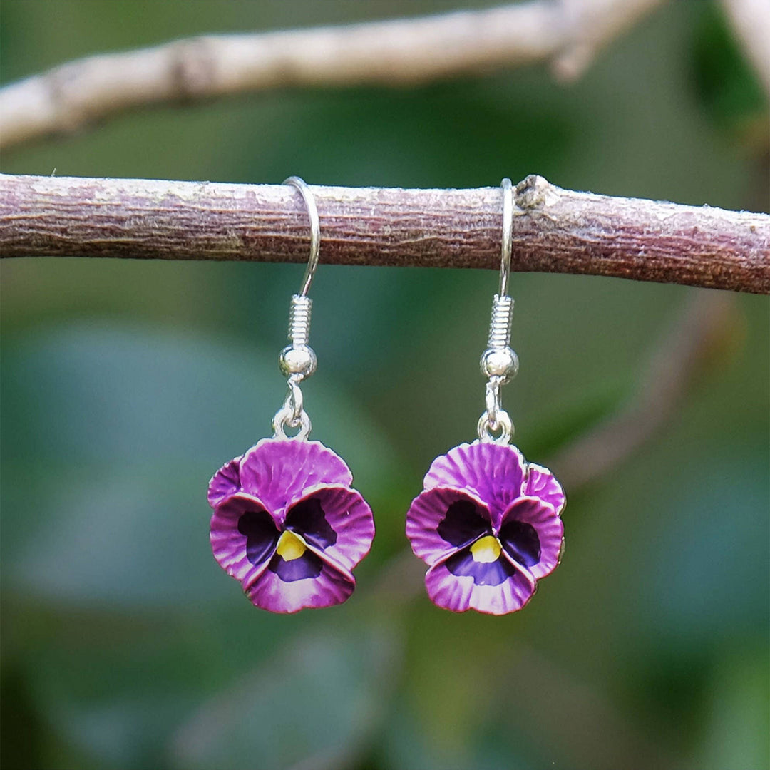 Purple flower-shaped earrings hanging from a branch with a blurred green background