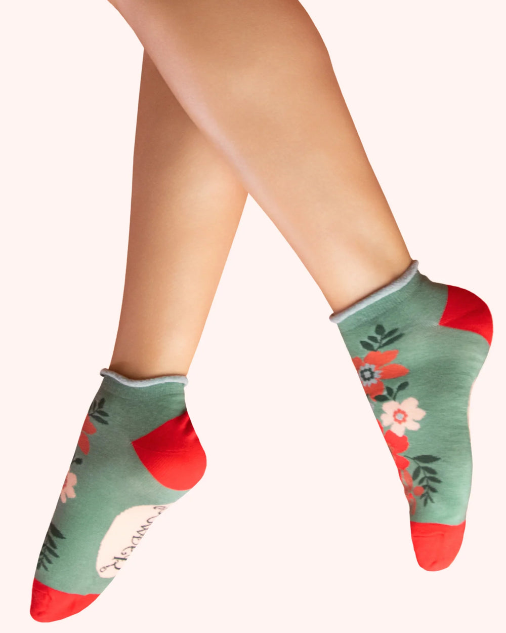 Green socks with floral pattern and red accents worn by a person on a white background