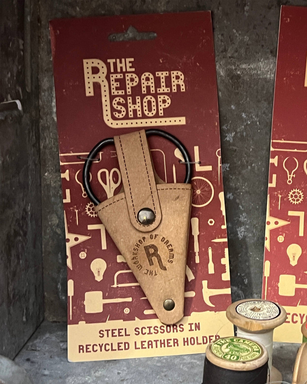 Steel scissors in a recycled leather holder from 'The Repair Shop' on a patterned background.