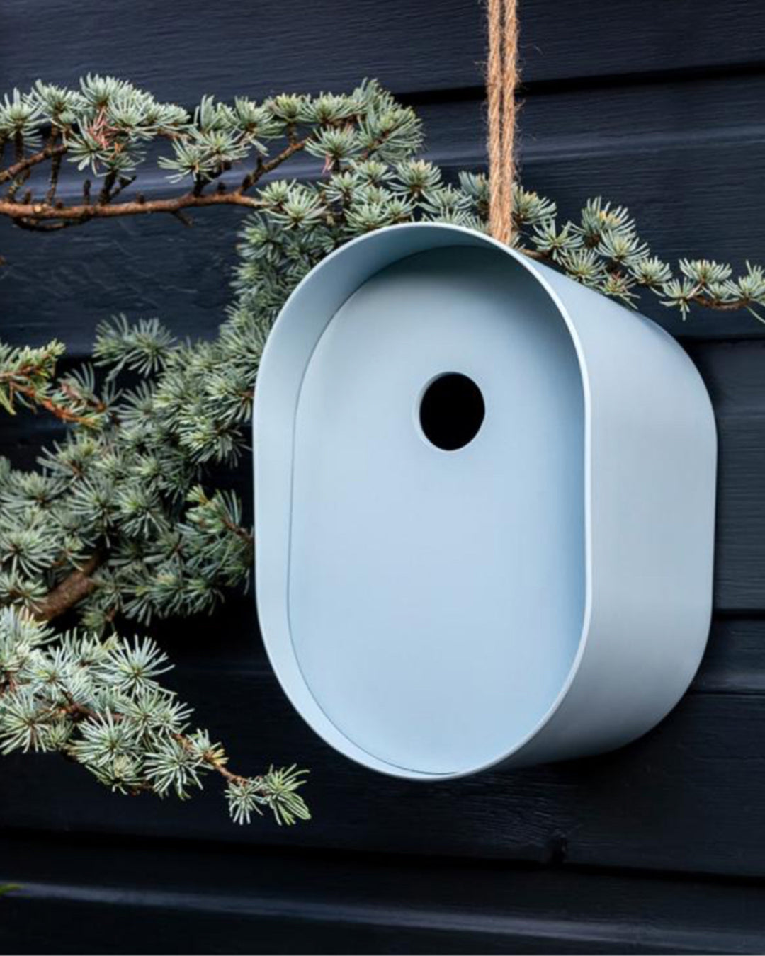 White birdhouse hanging on a branch with greenery