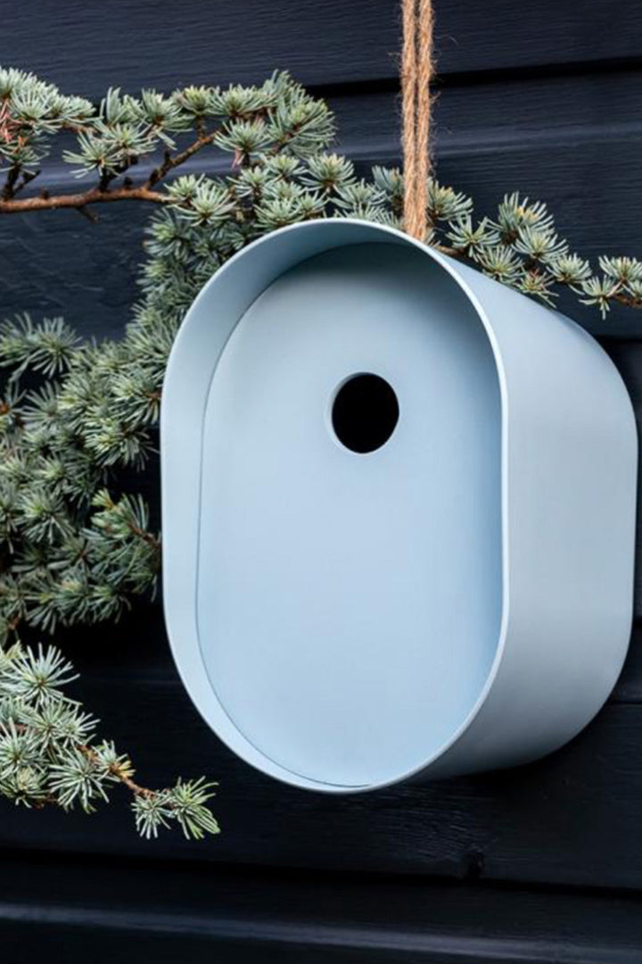 Light blue birdhouse hanging on a dark surface with green foliage.