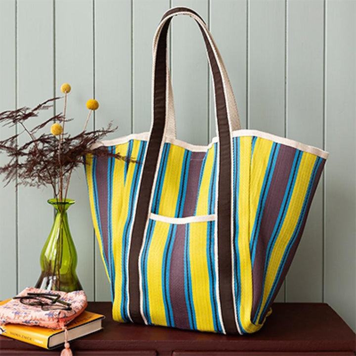 Striped tote bag with a green vase and books on a wooden surface