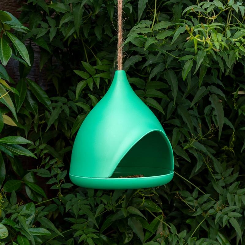 Green bird feeder hanging among green foliage