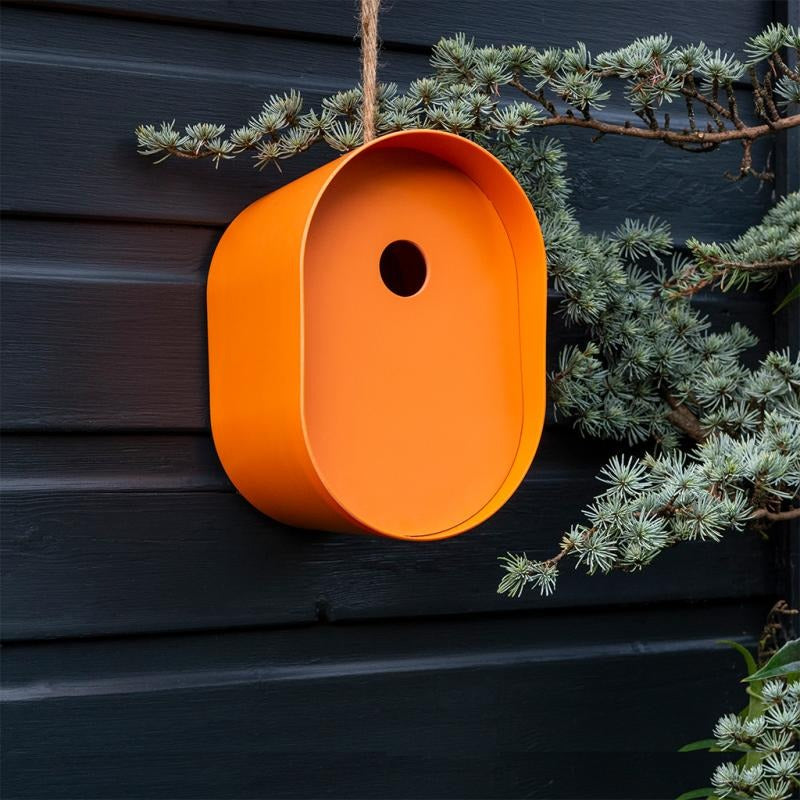 Orange birdhouse hanging on a branch against a dark wooden wall