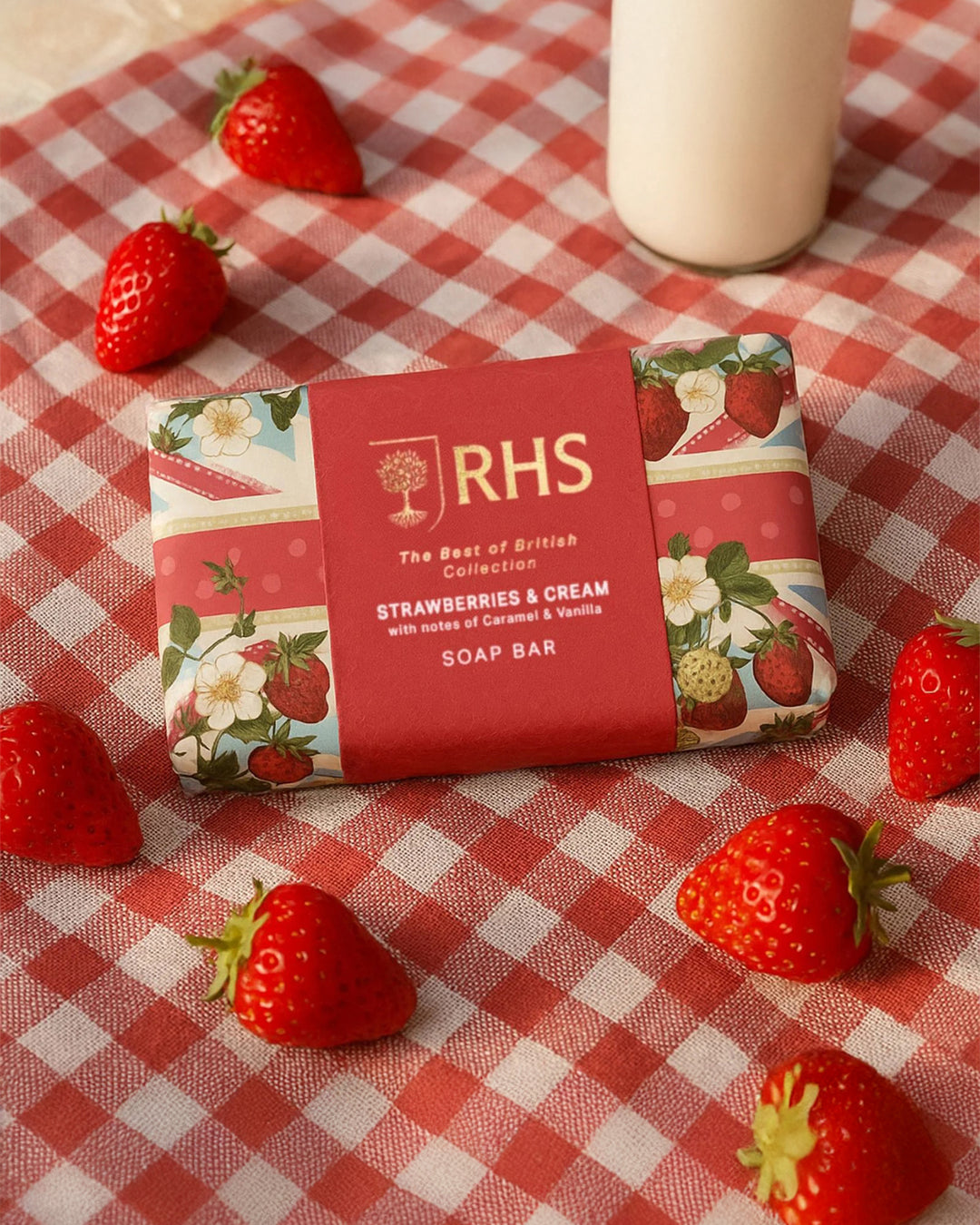 Soap bar with 'RHS' branding on a red and white checkered tablecloth with strawberries around it.