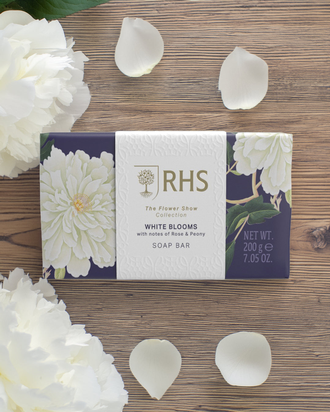 Soap bar with 'RHS' branding on a wooden surface with white flowers and petals.