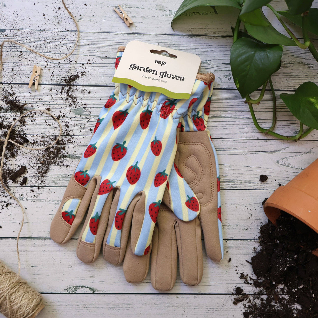 Gardening gloves with strawberry pattern on a wooden surface with gardening tools.