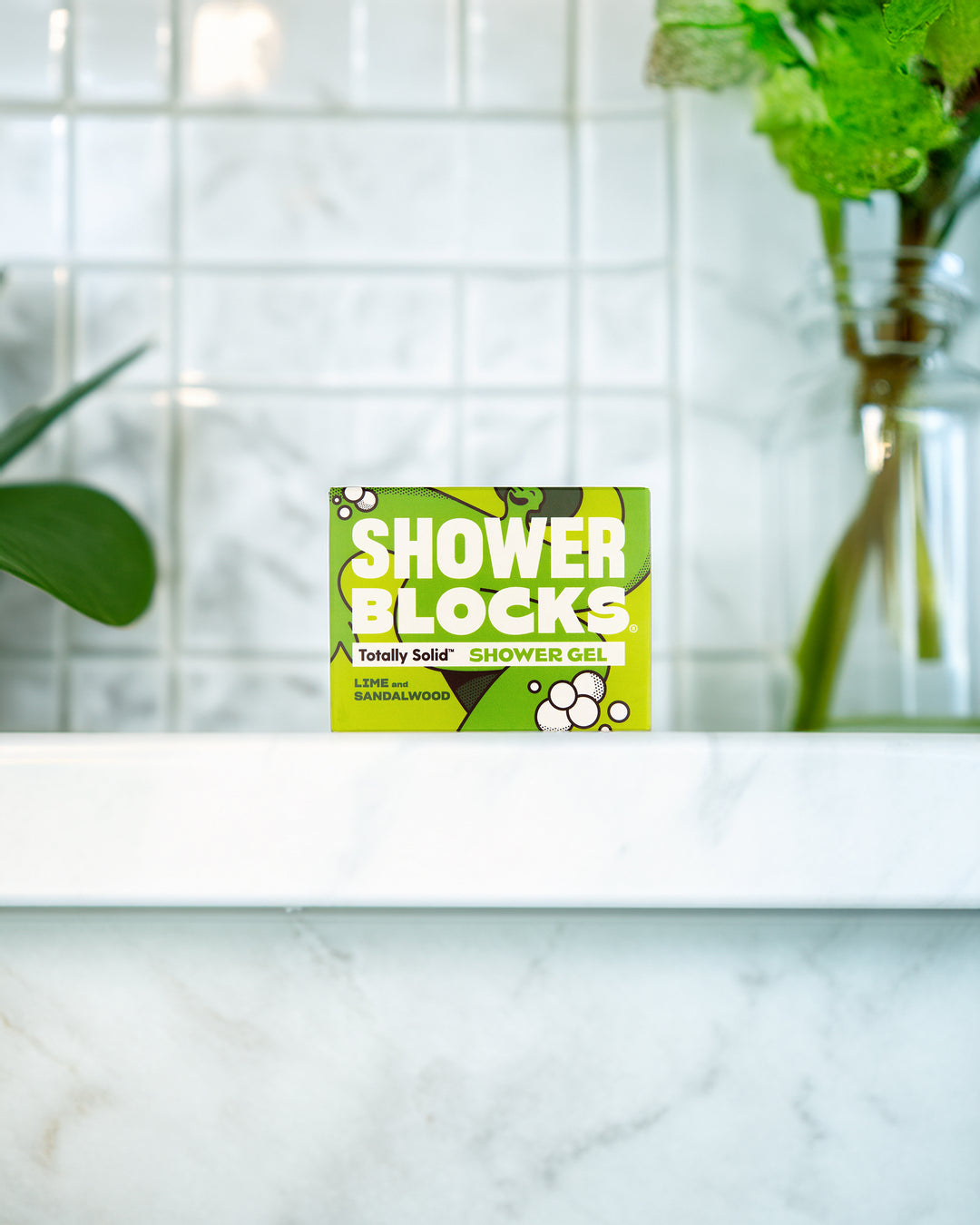 Shower Blocks packaging on a bathroom counter with a tiled wall and plant in the background