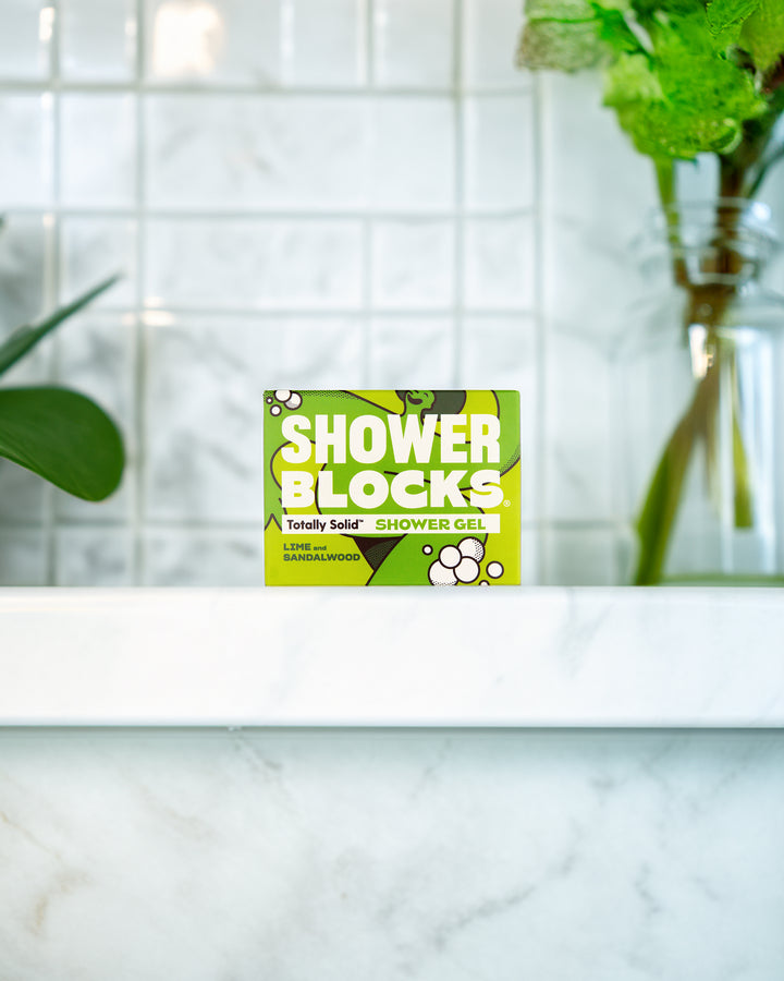 Shower Blocks packaging on a bathroom counter with a tiled wall and plant in the background