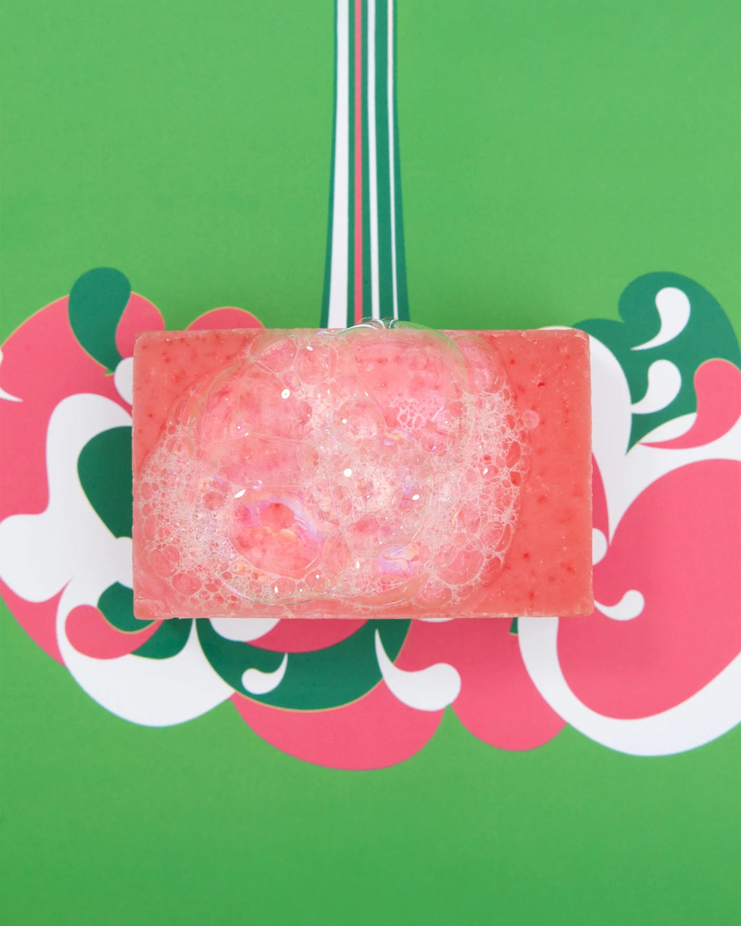 Pink soap bar with bubbles on a decorative card with floral patterns against a green background