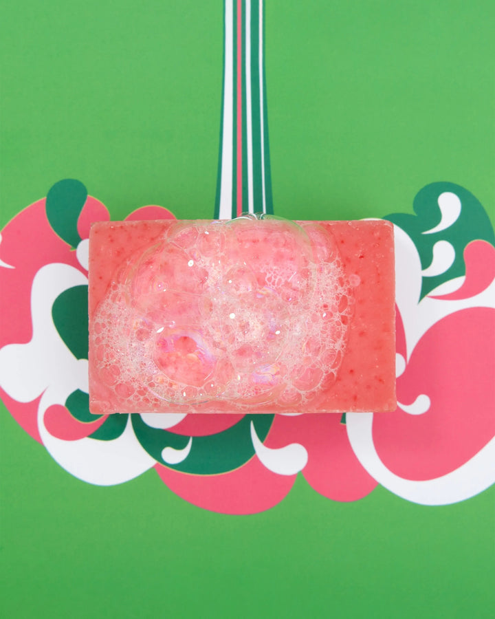 Pink soap bar with bubbles on a decorative card with floral patterns against a green background