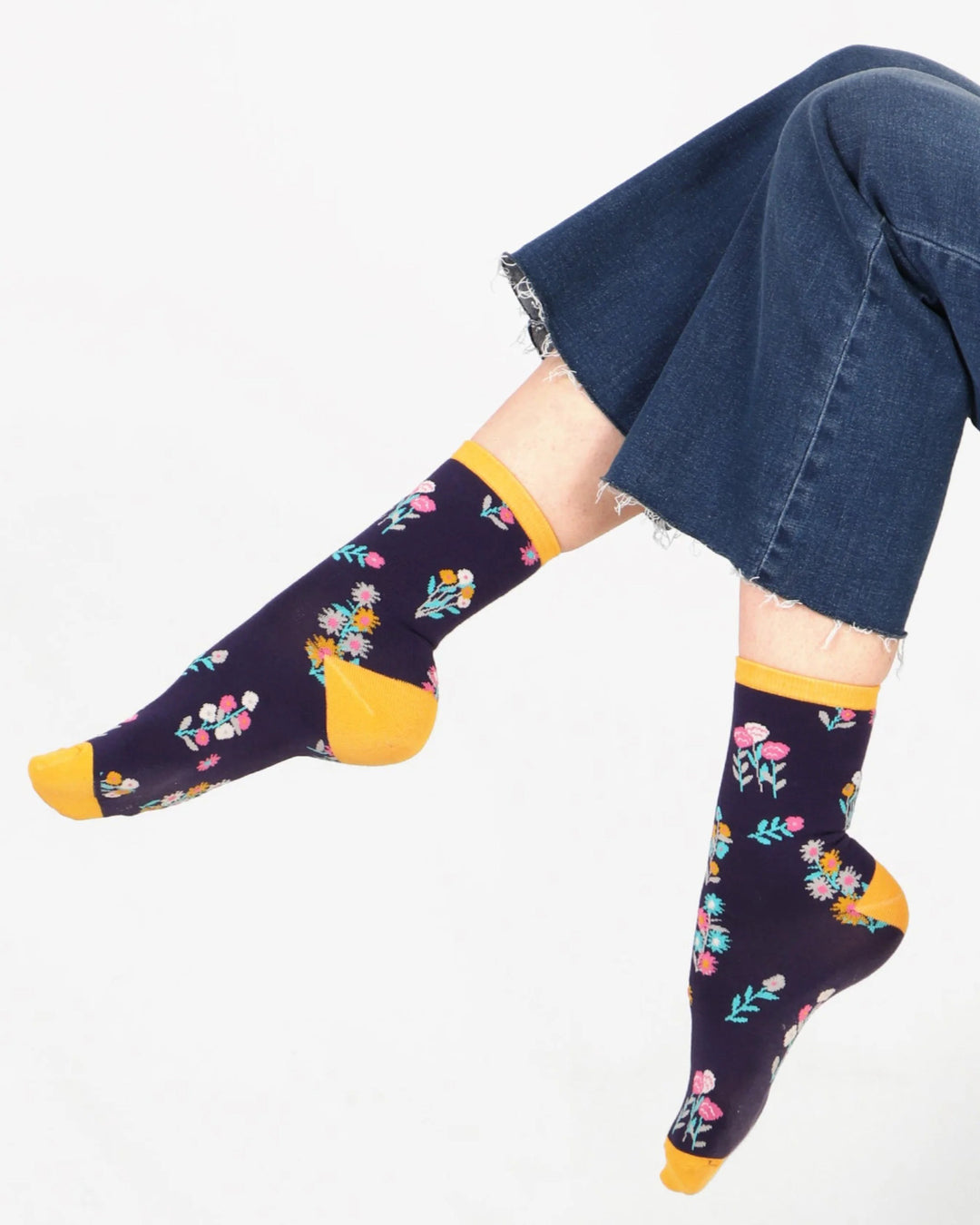 Navy socks with floral pattern and yellow toes worn with blue jeans on a white background