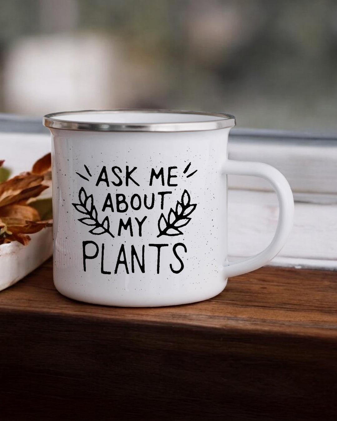 White mug with 'Ask me about my plants' text on a wooden surface.