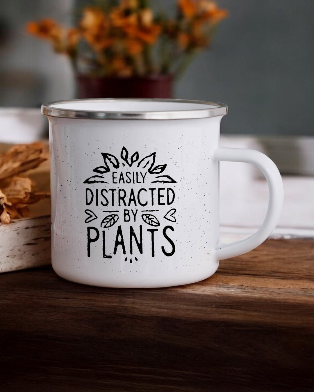 White mug with 'Easily Distracted by Plants' text on a wooden surface with flowers in the background