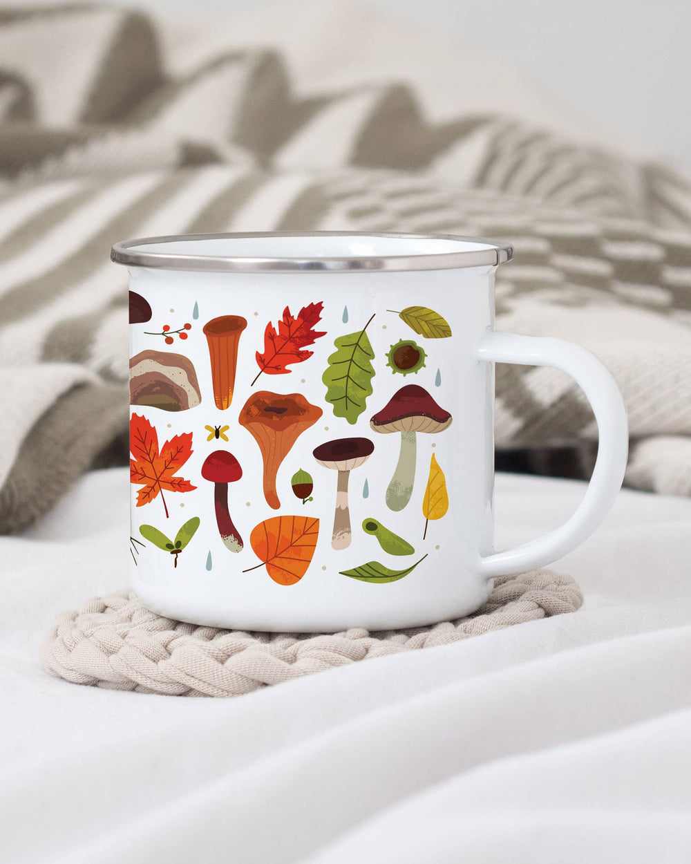 White mug with autumn-themed design featuring mushrooms and leaves on a textured surface.