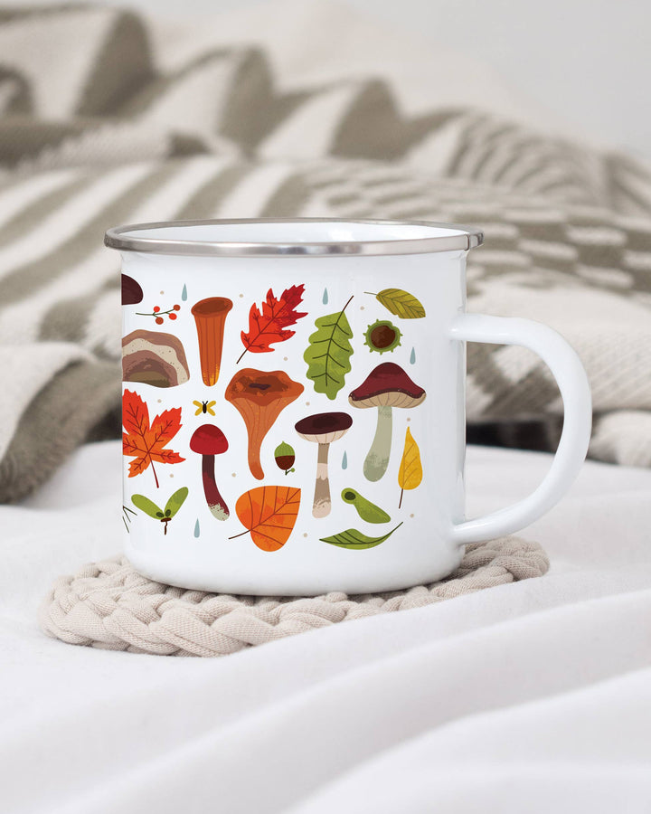 White mug with autumn-themed design featuring mushrooms and leaves on a textured surface.