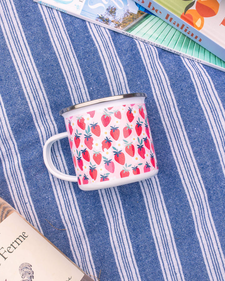 Enamel mug with strawberry pattern on a blue striped fabric background