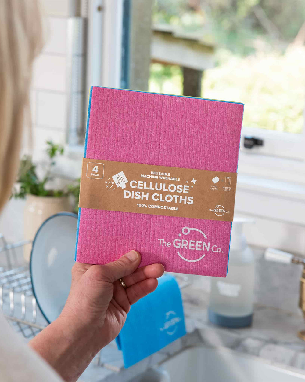 Person holding a package of The Green Co. cellulose dish cloths in a kitchen setting.