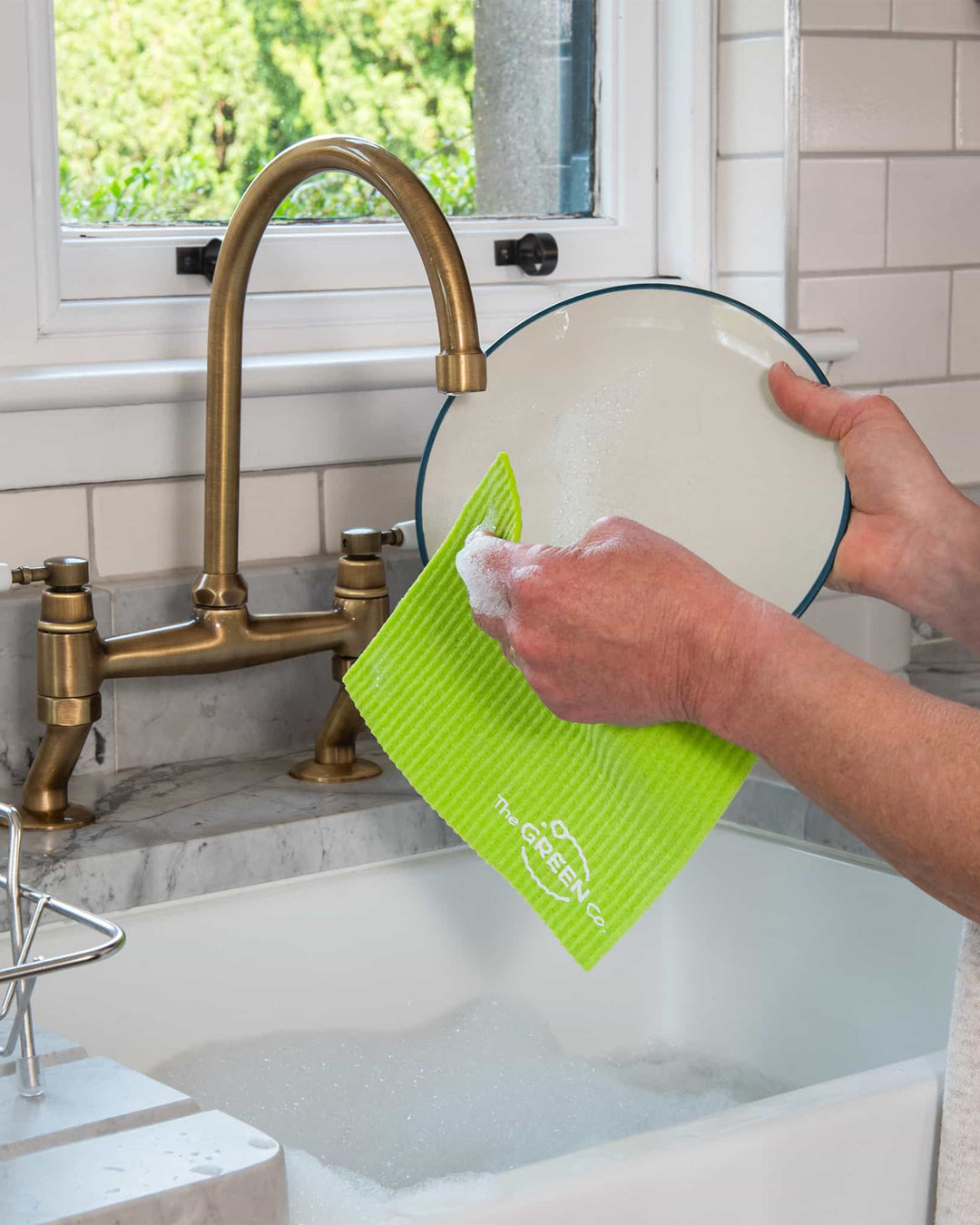 Person washing a plate with a green sponge in a kitchen sink.