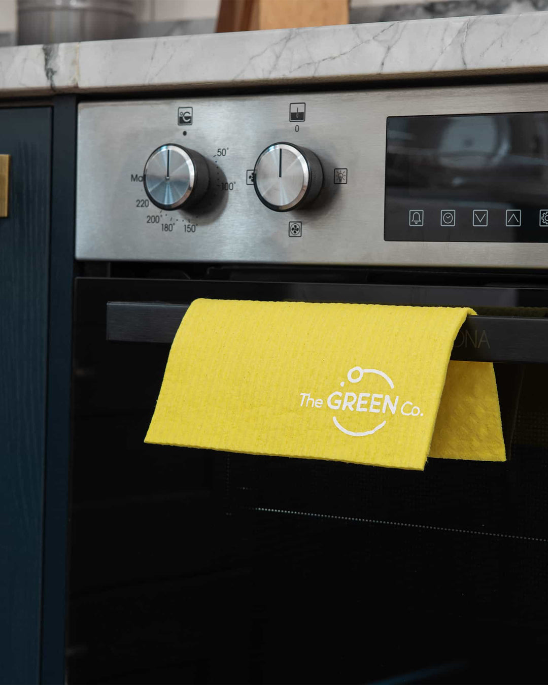 Yellow towel with 'The GREEN Co.' logo hanging on a kitchen oven.