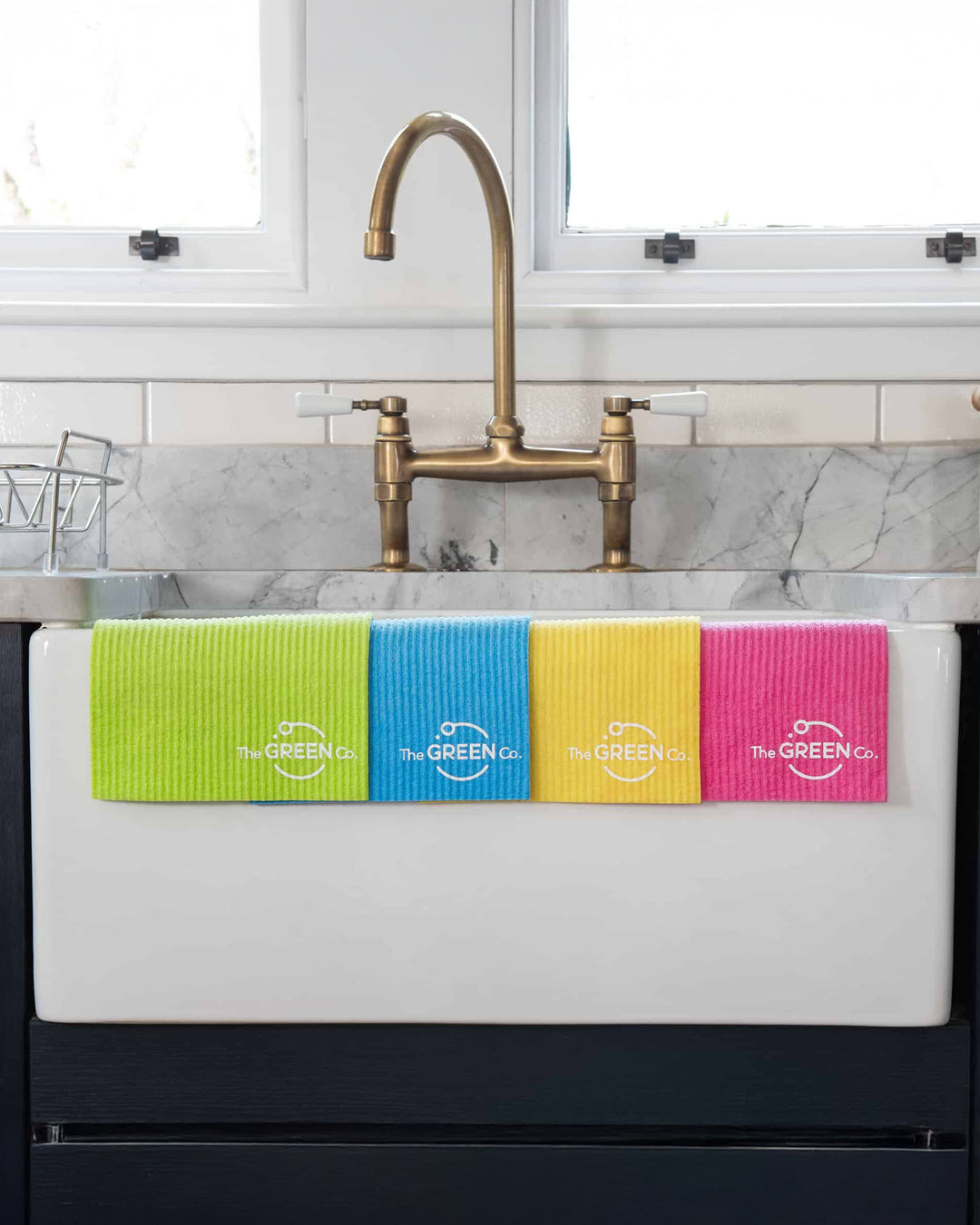 Four colorful towels hanging on a kitchen sink with 'The Green Co.' branding.