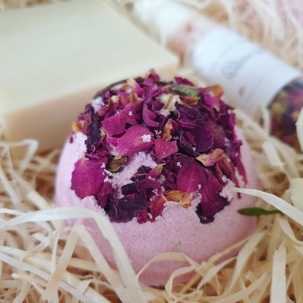 Pink bath bomb with purple flower petals on a bed of straw