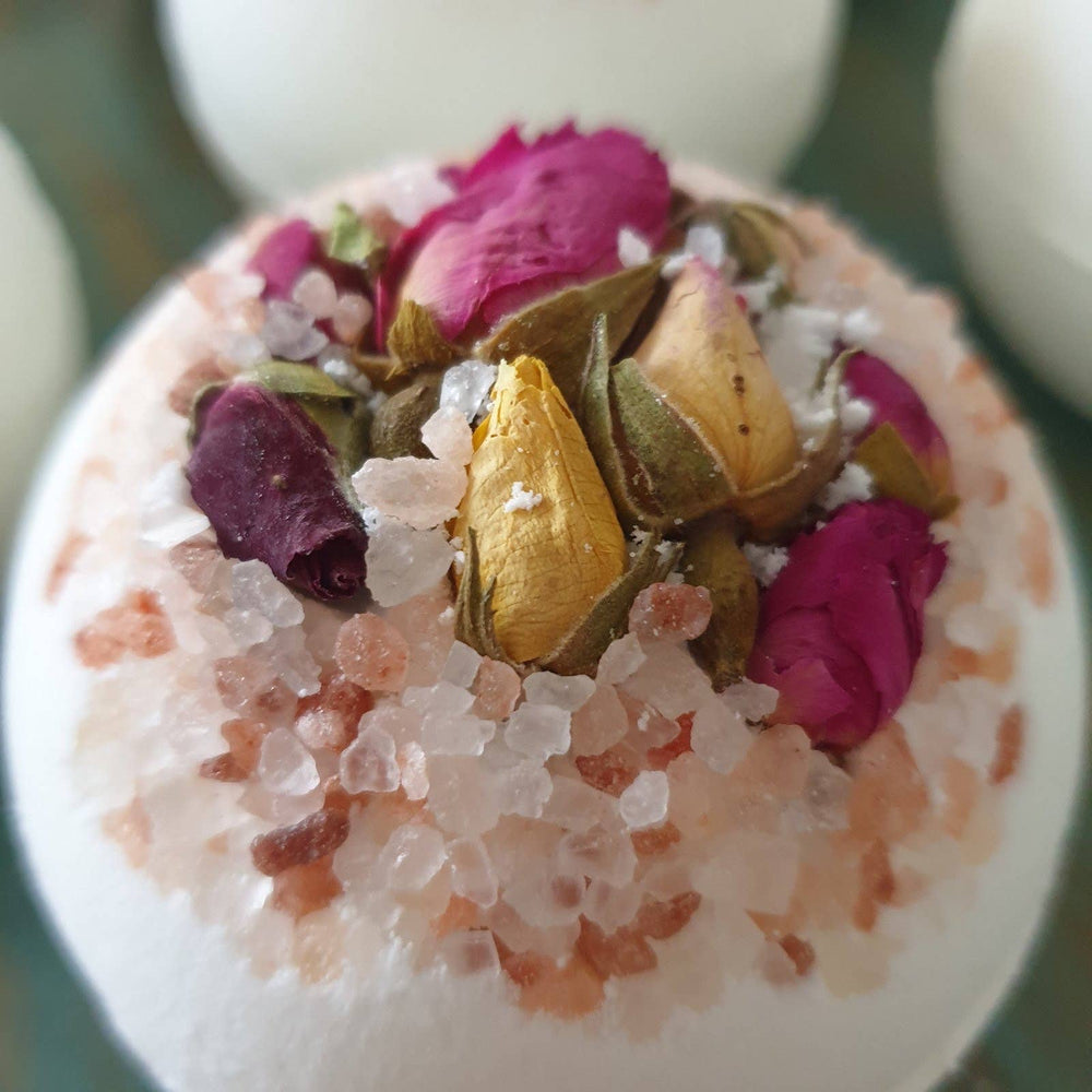 Bath bomb with pink and gold flower petals on a white background