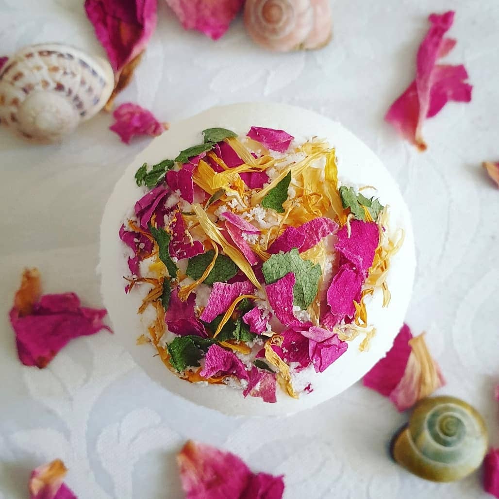 Bath bomb with colorful petals on a white surface with seashells and petals around