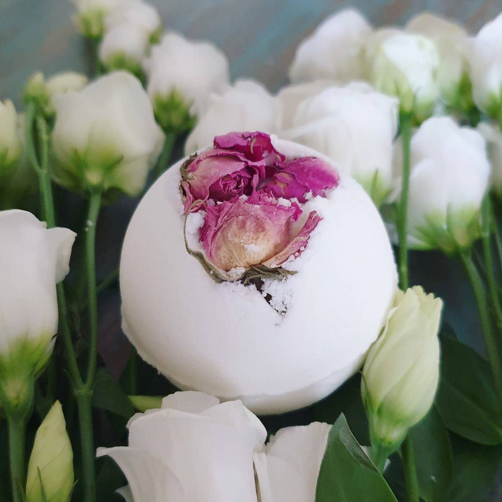 White bath bomb with a pink flower inside, surrounded by white flowers.