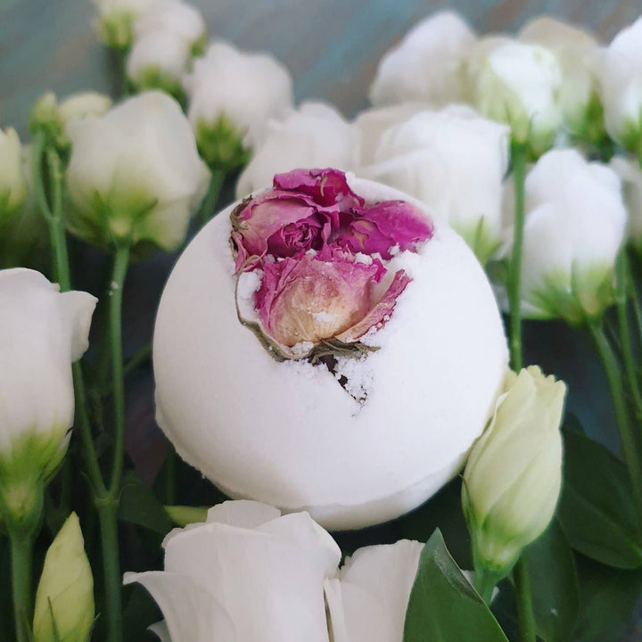 White bath bomb with a pink flower inside, surrounded by white flowers.