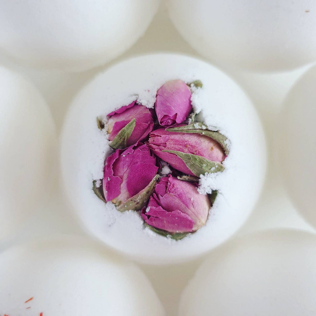 White bath bomb with pink rose petals and green leaves on a white background