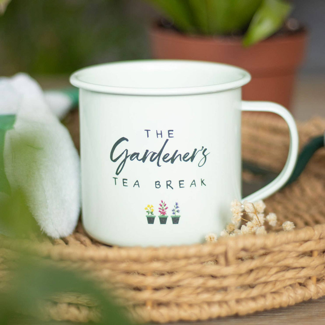 White mug with 'The Gardener's Tea Break' text on a woven mat with plants in the background