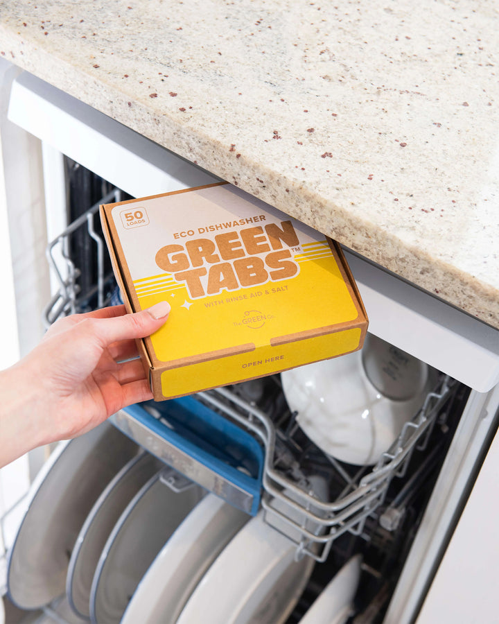 Box of Green Tabs dishwasher tablets held above an open dishwasher.