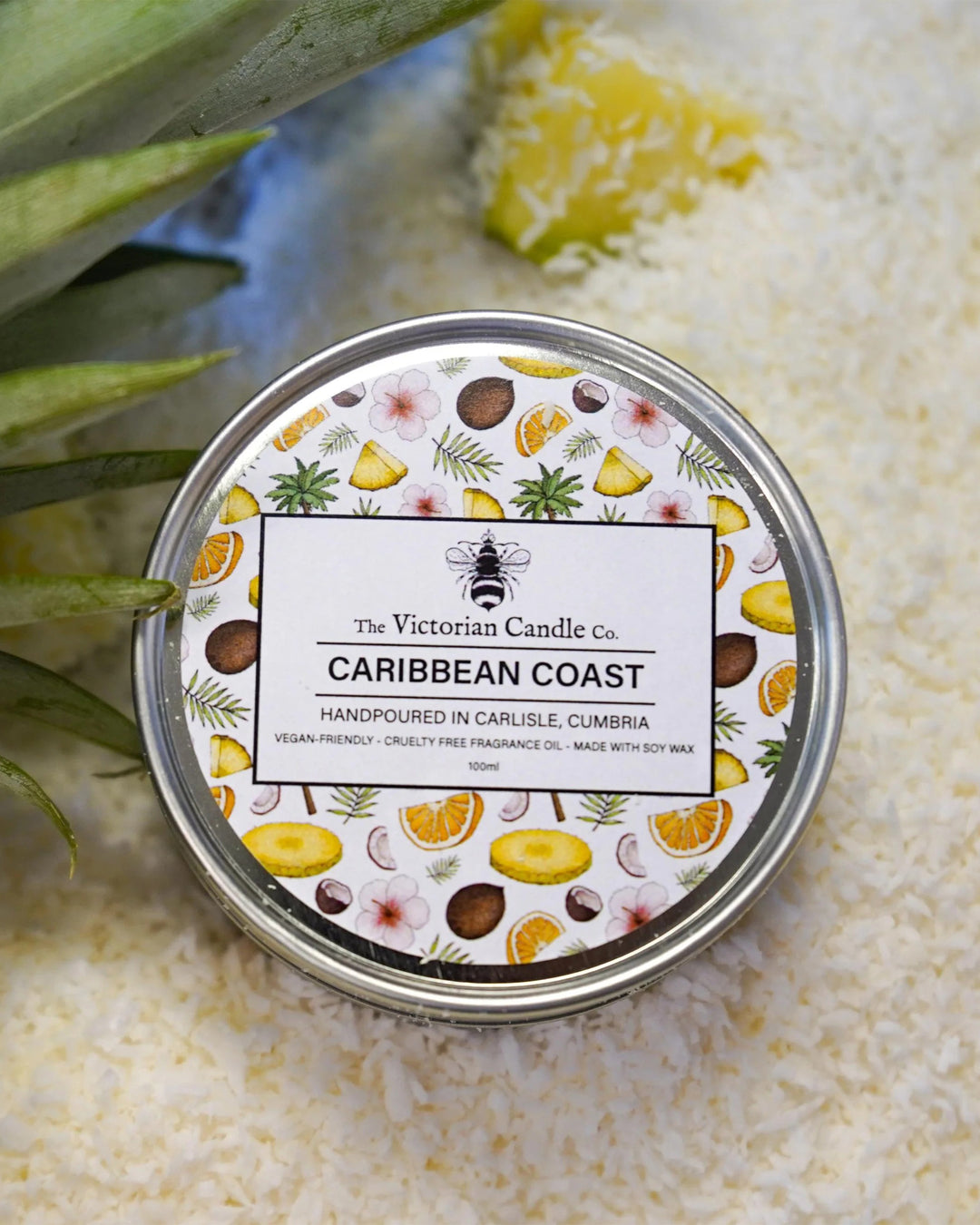 Candle tin labeled 'Caribbean Coast' by The Victorian Candle Co. on a textured surface with leaves.