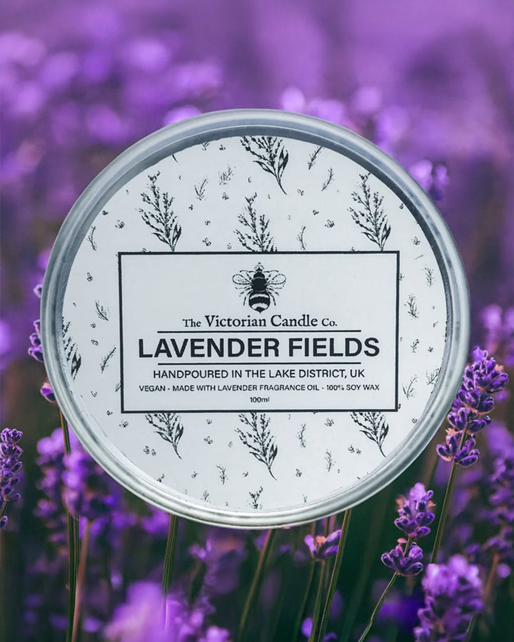 Candle tin labeled 'Lavender Fields' by The Victorian Candle Co. surrounded by lavender flowers.