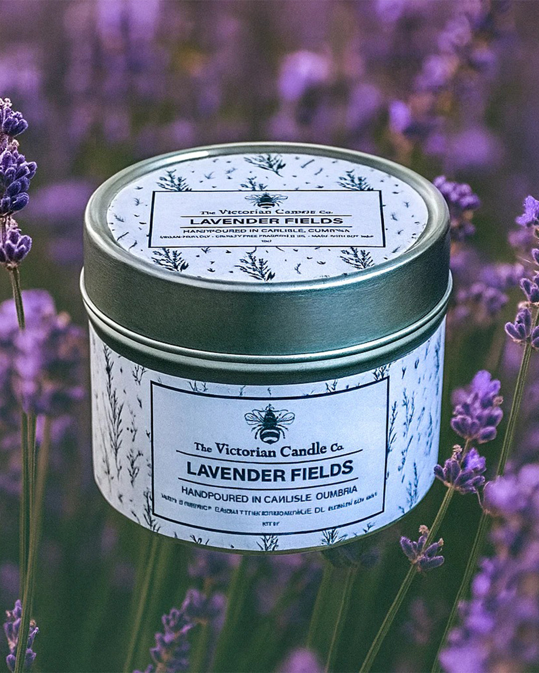 Candle tin labeled 'Lavender Fields' by The Victorian Candle Co. surrounded by lavender flowers.