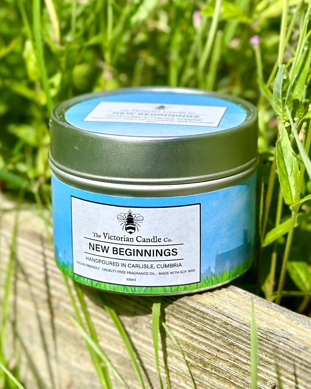 Candle jar labeled 'New Beginnings' by The Victorian Candle Co. on a grassy background