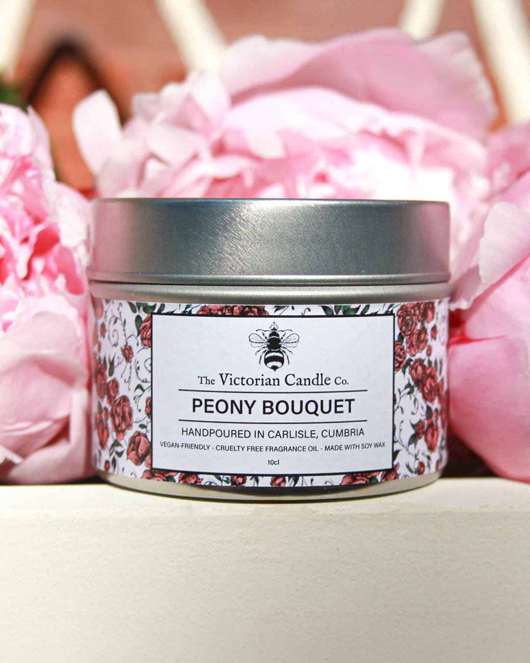 Candle jar labeled 'Peony Bouquet' from The Victorian Candle Co. with pink flowers in the background.