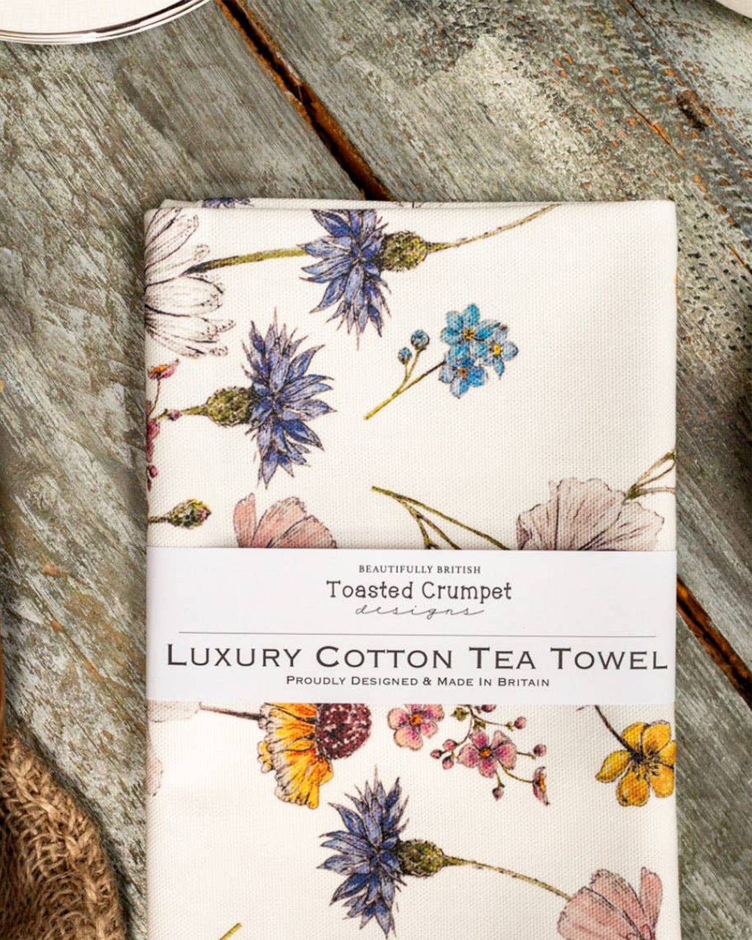 Floral patterned tea towel on a wooden surface with 'Toasted Crumpet' branding.