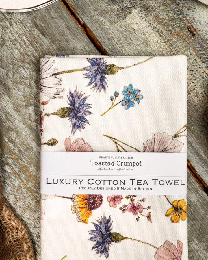 Floral patterned tea towel on a wooden surface with 'Toasted Crumpet' branding.
