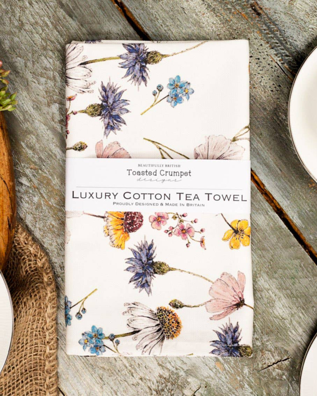 Floral patterned tea towel on a wooden surface with 'Toasted Crumpet' branding.