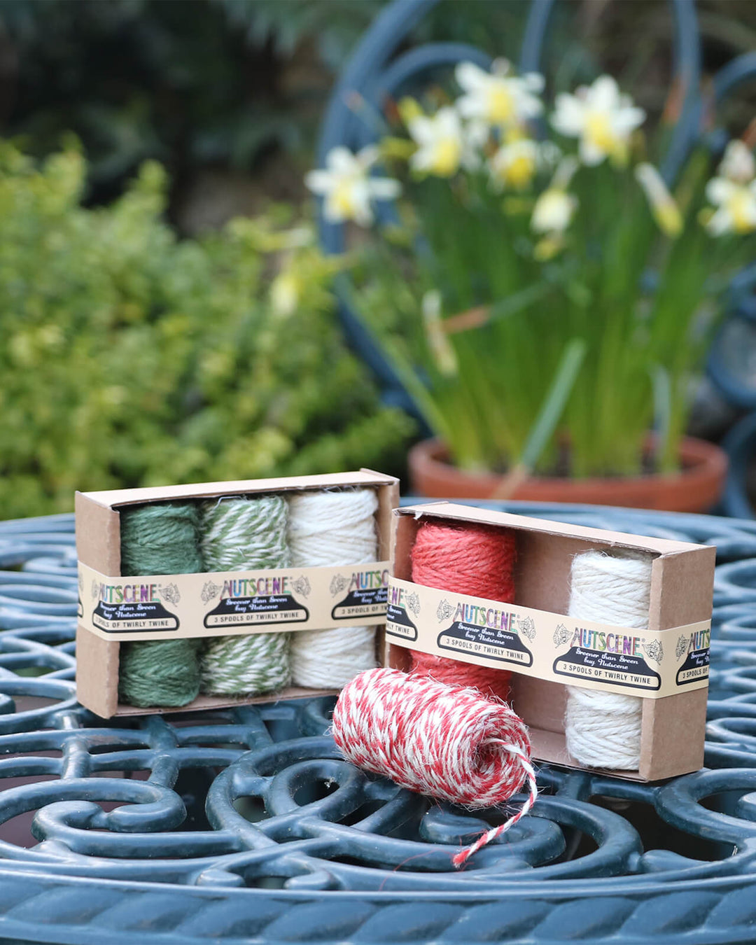 Two boxes of nutscene yarn on a patio table with flowers in the background