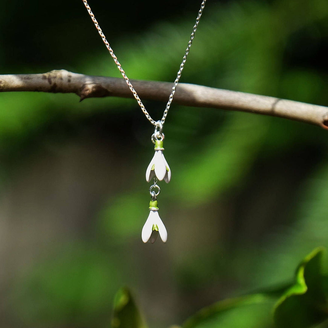 Necklace with floral pendants hanging on a branch against a natural background