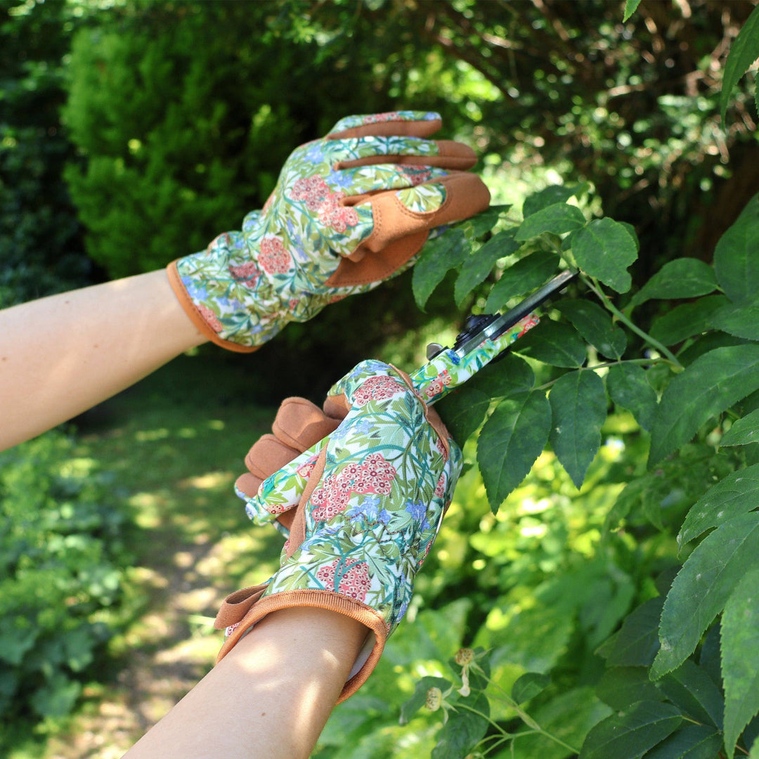 Person wearing floral gardening gloves trimming a bush outdoors.