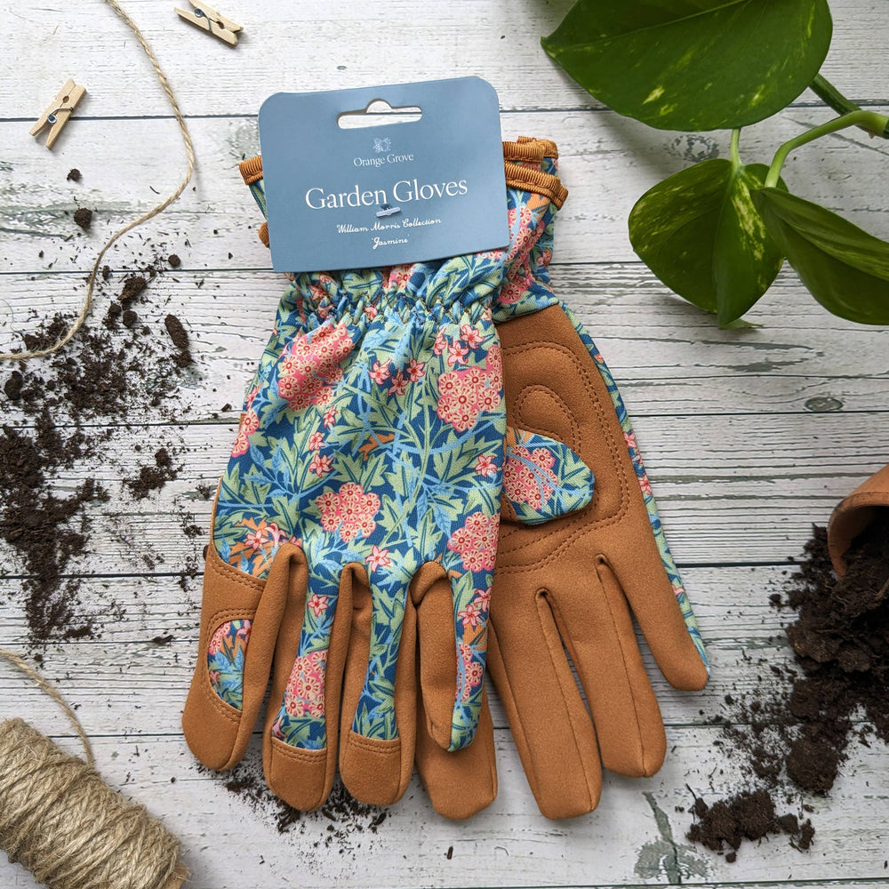 Pair of floral gardening gloves on a wooden surface with soil and plants.