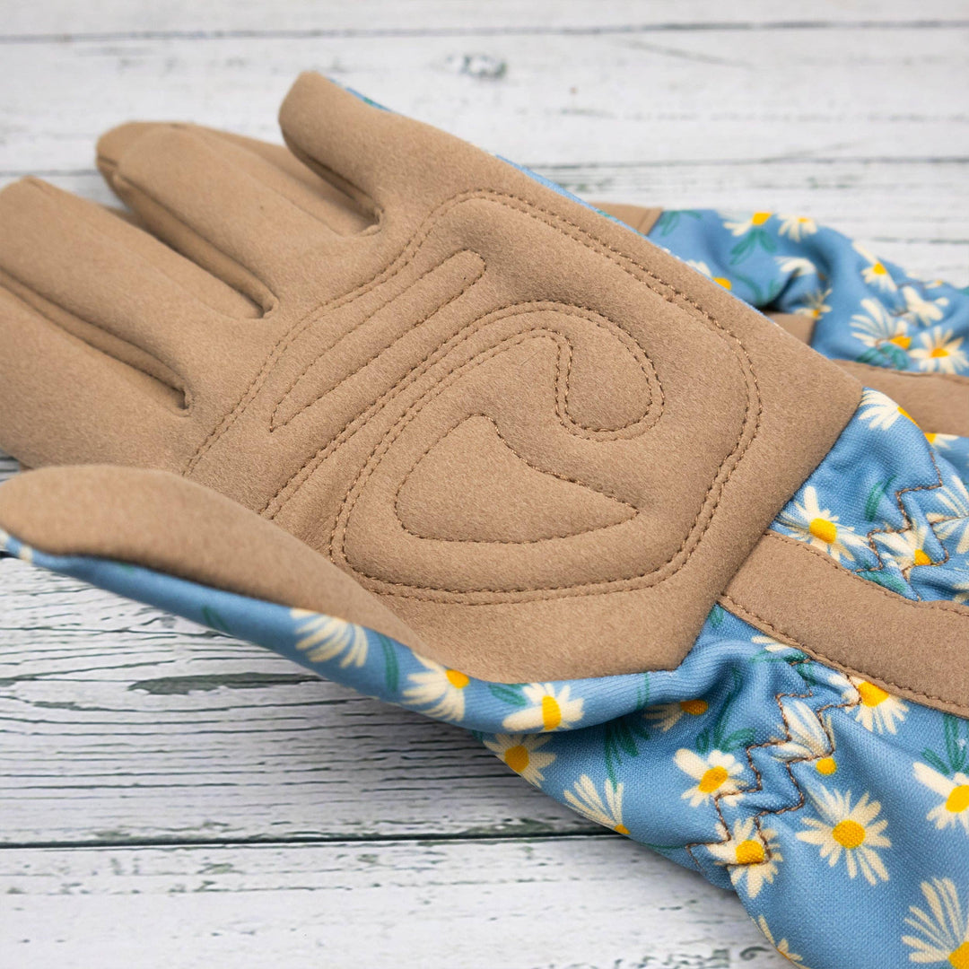 Pair of gloves with tan palm and blue floral cuff on a wooden surface