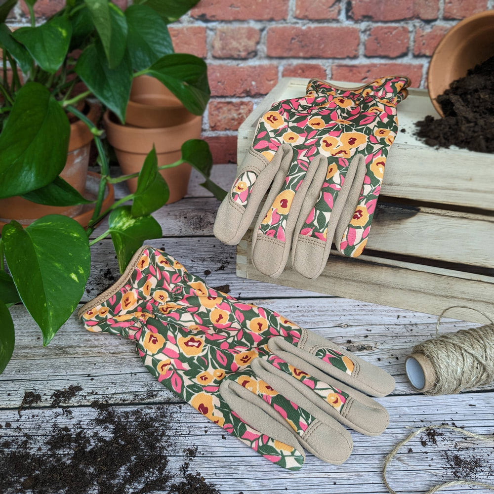 Floral gardening gloves on a wooden surface with plants and tools in the background