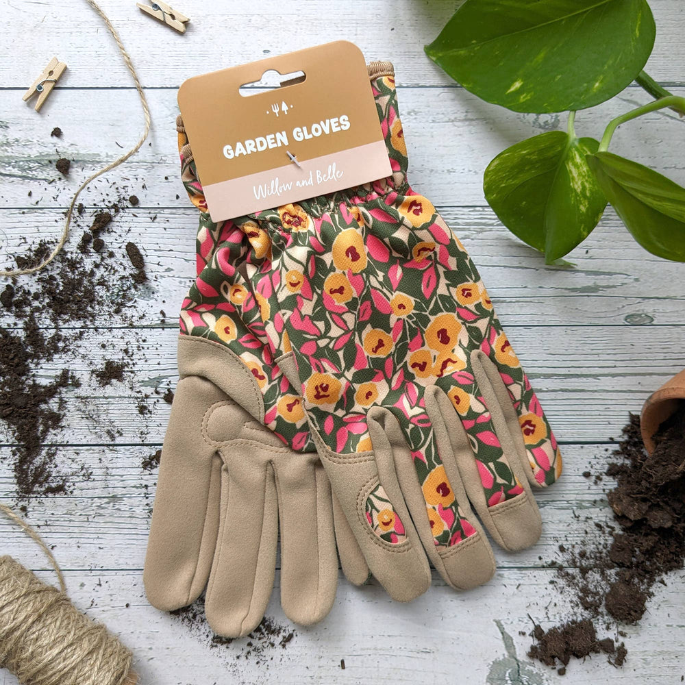 Floral gardening gloves on a wooden surface with gardening tools and plants.