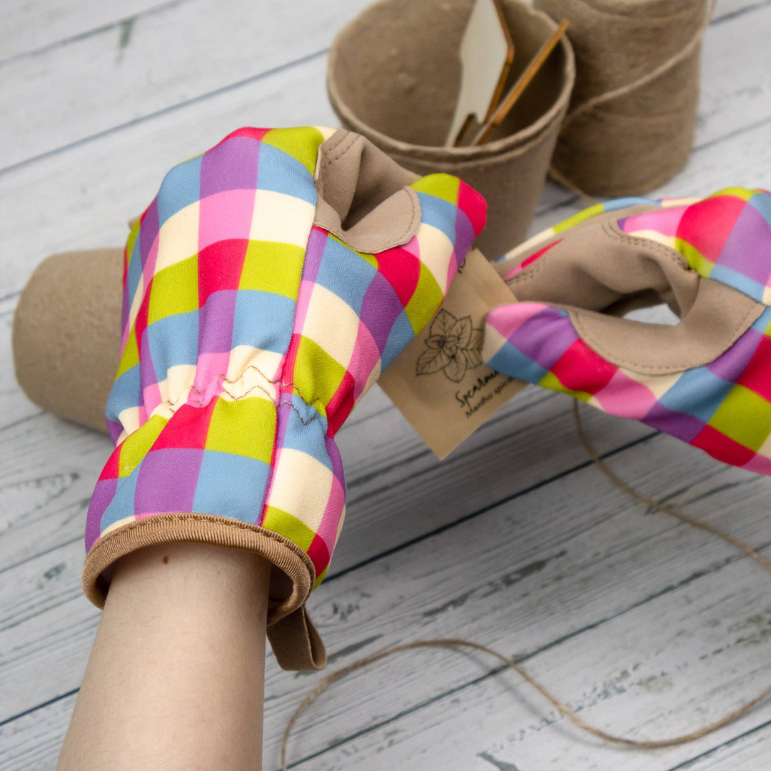 Colorful checkered oven mitts on a wooden surface with a brand tag.